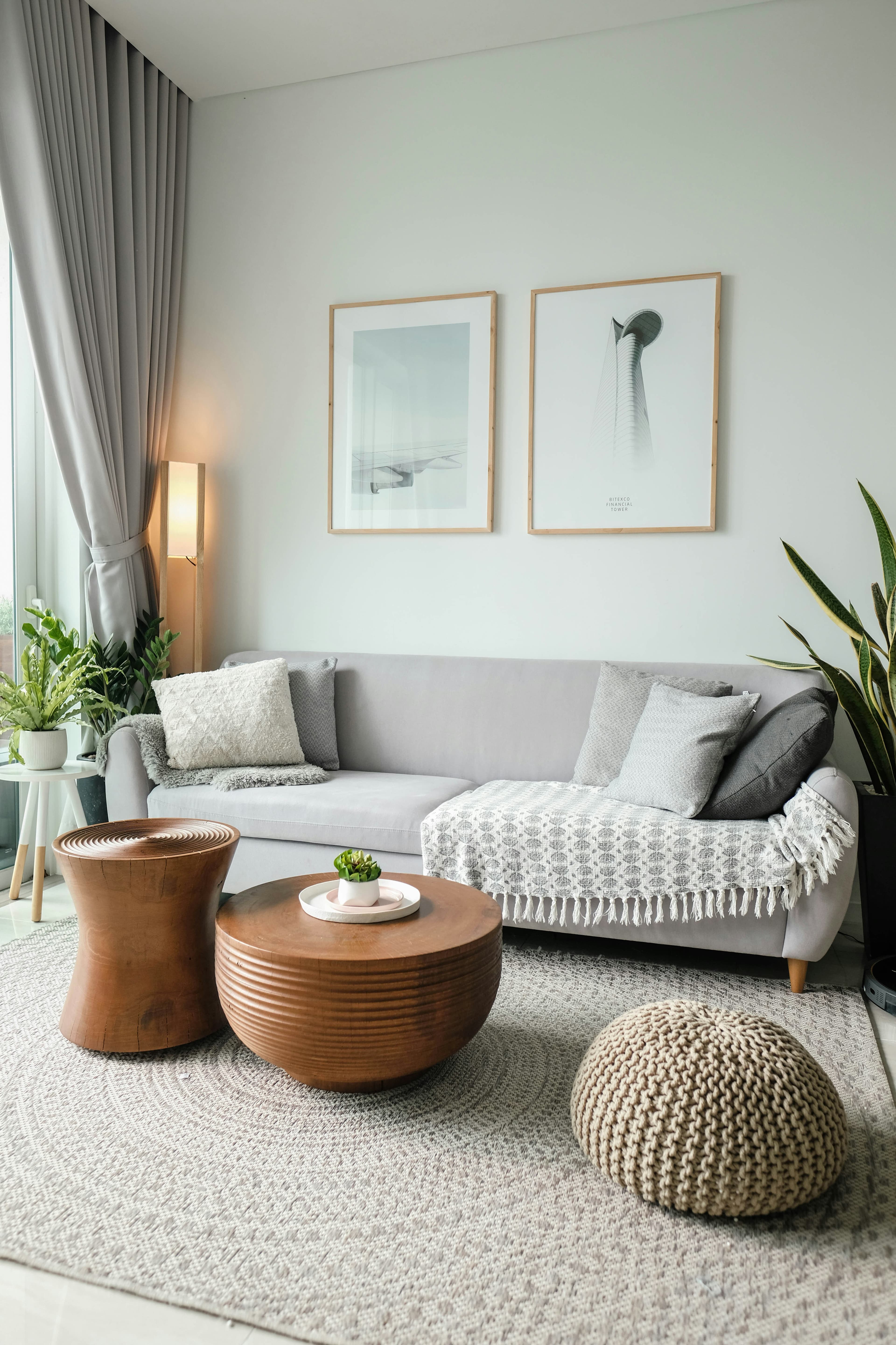 Helles, wohnliches Wohnzimmer mit grauem Sofa, Kissen, Holzmöbeln und Grünpflanzen